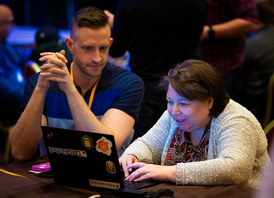 An AWS associate watching an attendee learn something new on a laptop