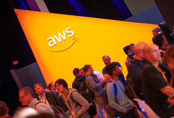 A crowd of people in front of an orange wall with an AWS logo